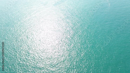 Shimmering turquoise ocean reveals stunning aerial view of maritime infrastructure featuring bright sunlight reflecting off Containers and global shipping vessels amidst expansive blue waters.