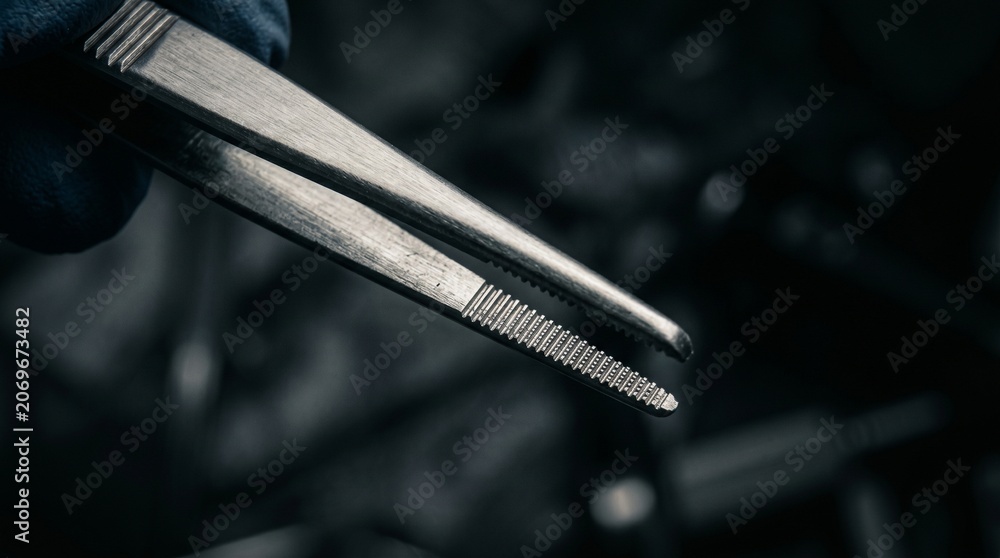 Naklejka premium Surgical forceps held by a doctor or surgeon in a moody, cinematic operating room setting.