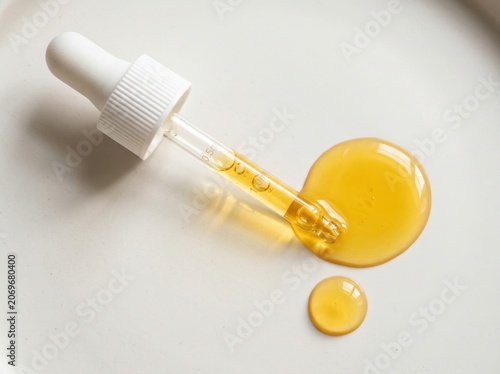 Glass dropper dispensing viscous golden oil serum for skincare and beauty applications