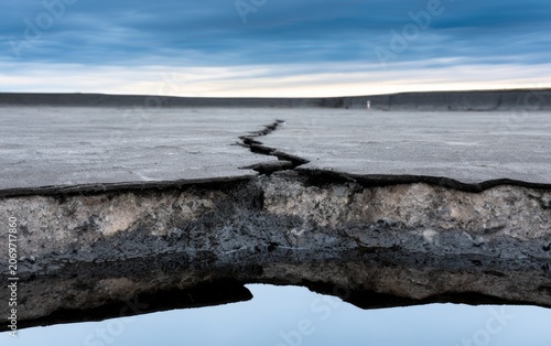 Close-Up of Weathered Flat Roof with Visible Cracks and Reflection on Calm Surface in Dramatic Sky