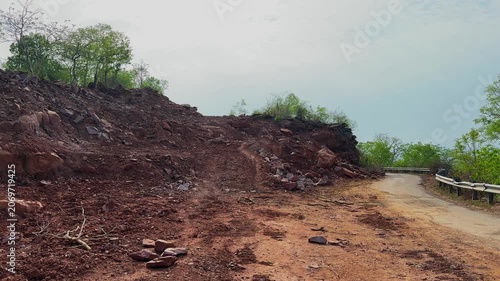Tracking shot along a forest road widening project showing exposed earth cut slopes removed vegetation and altered terrain The scene documents infrastructure development and landscape transformation
