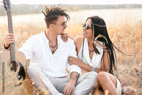 Foto Young couple of hippies with dreadlocks and guitar sitting outdoors