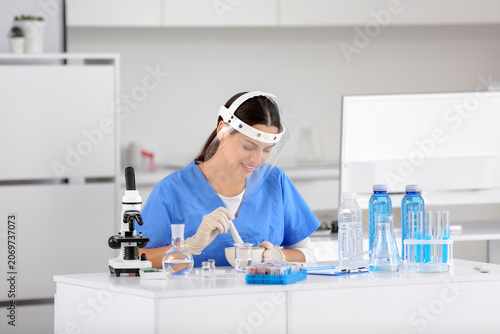 Happy female young scientist with mortar and pestle examining water quality i...