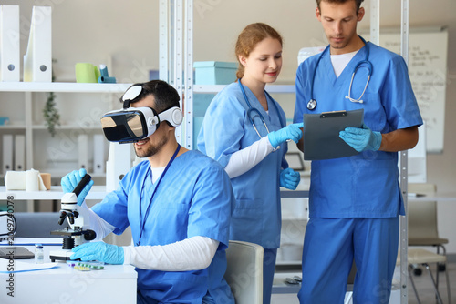 Male doctor with microscope using VR glasses at table in clinic