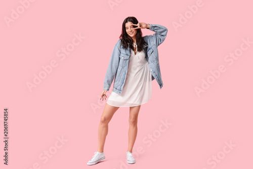 Foto Beautiful young woman in stylish white dress dancing and showing victory gesture