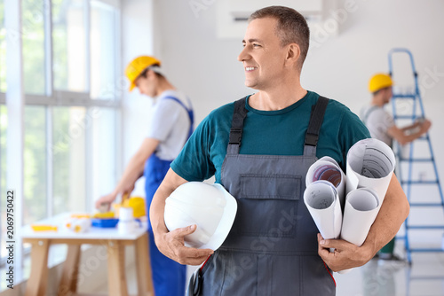 Mature builder with hardhat and paper rolls in room