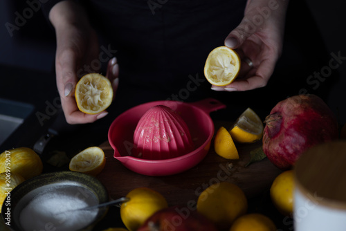 Female Hands Squeezing Fresh Lemons with Manual Juicer and Pomegranate with Selective Focus