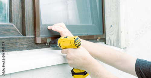 Hands hold drill near window screen