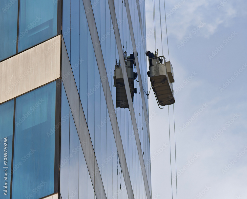Obraz premium Workers on suspended platforms clean high-rise building windows