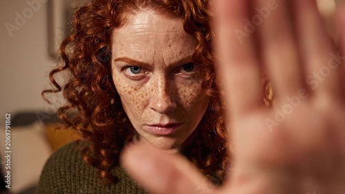 Serious redhead woman holding her hand up in a stop gesture at home