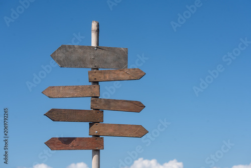 Obraz na plátně Wooden signpost with blank arrows pointing in different directions against a cle