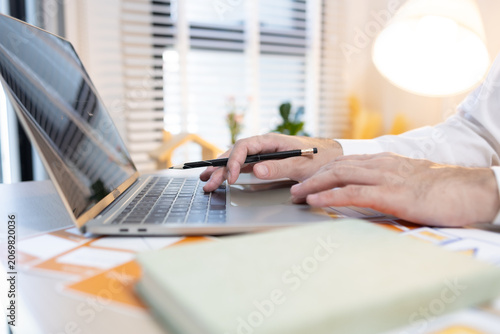 Man works at desk with laptop and blueprints. Hands tap keyboard while reviewing plans. Soft light glows behind workspace. Focused on task, calm and professional. Ideal for business, architecture
