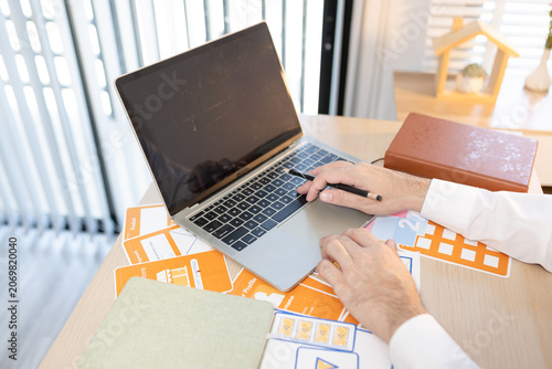 Man works at desk with laptop and blueprints. Hands tap keyboard while reviewing plans. Soft light glows behind workspace. Focused on task, calm and professional. Ideal for business, architecture
