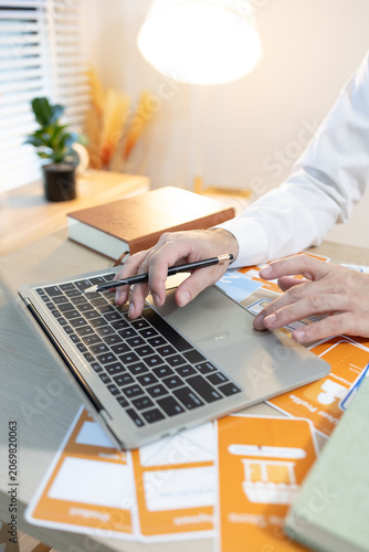 Man works at desk with laptop and blueprints. Hands tap keyboard while reviewing plans. Soft light glows behind workspace. Focused on task, calm and professional. Ideal for business, architecture
