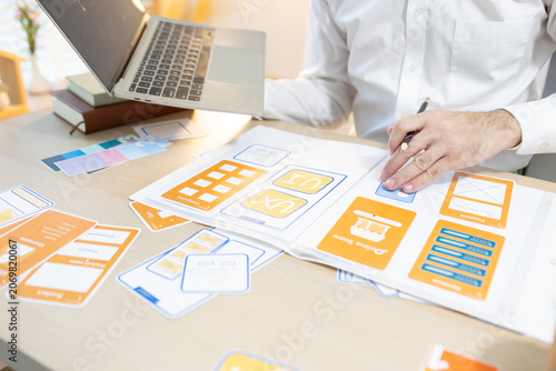 Man works at desk with laptop and blueprints. Hands tap keyboard while reviewing plans. Soft light glows behind workspace. Focused on task, calm and professional. Ideal for business, architecture
