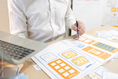 Man works at desk with laptop and blueprints. Hands tap keyboard while reviewing plans. Soft light glows behind workspace. Focused on task, calm and professional. Ideal for business, architecture
