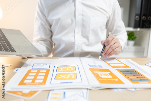 Man works at desk with laptop and blueprints. Hands tap keyboard while reviewing plans. Soft light glows behind workspace. Focused on task, calm and professional. Ideal for business, architecture
