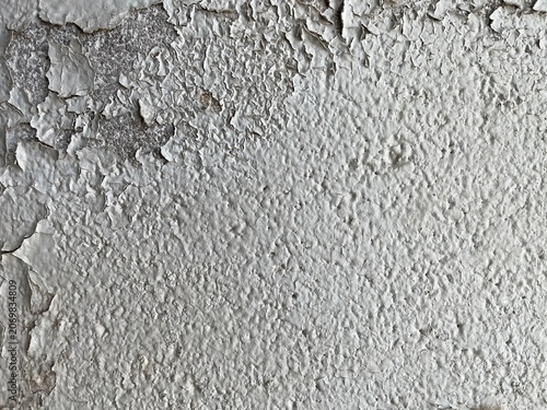 Abstract white peeling paint texture background with cracked surface. Close up of peeling white paint and damaged plaster on concrete wall. Paint falling off from a brick concret wall.