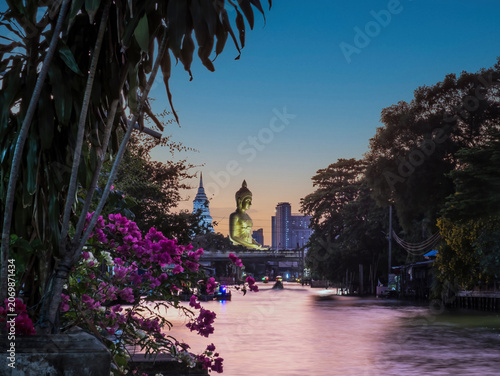 View of big Buddha statue in Bangkok, Thailand (Wat Pak Nam Phasi Charoen) from canal with wooden houses and long tails boats
