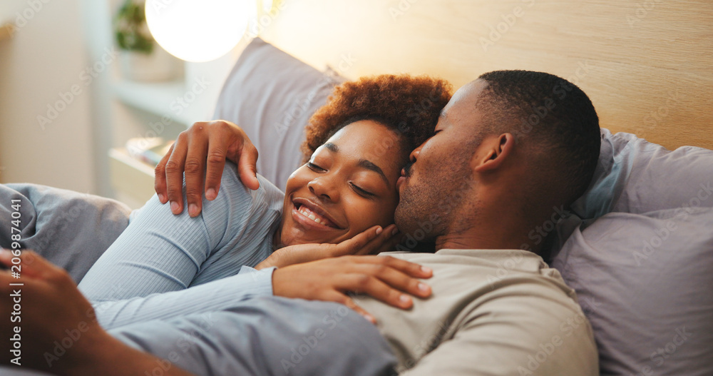 Fototapeta premium Kiss, love and relax with black couple in bed at apartment together for bonding, connection or rest. Affection, morning and wake up with happy people in bedroom of home for break, holiday or romance