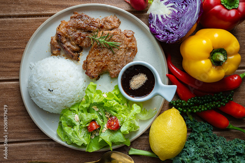Healthy balanced meal concept. Roasted pork with rice, salad, and colorful raw ingredients like bell pepper, kale, and chili around the plate.