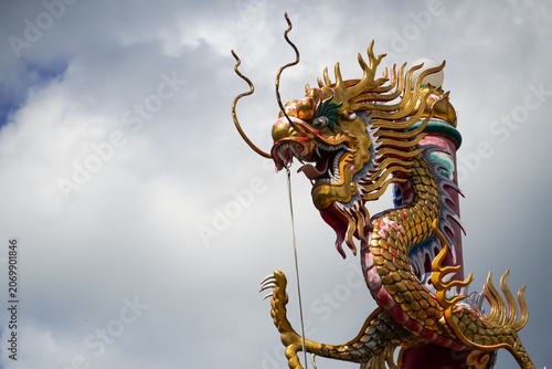 Ornate golden dragon statue with intricate scales against a cloudy sky