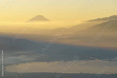 Golden morning mist and dramatic light beams over Lake Suwa with Mount Fuji rising above the clouds from Takabocchi Highlands in November, Japan.