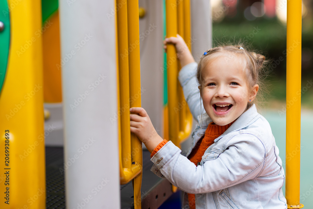 Fototapeta premium Smiling young girl playing on yellow bars at outdoor playground