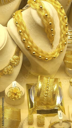 Close-up of ornate gold jewelry on display stands in a shop, featuring braided necklaces, bracelets, rings, and bangles with slight camera movement