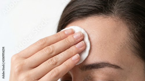 Closeup woman hand gently applies a cotton pad to cleaning makeup on her forehead with copy space on white background 