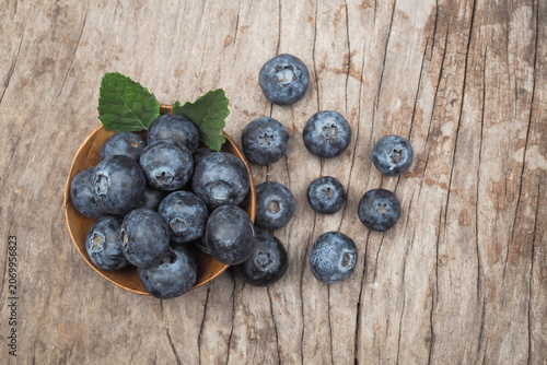 Top view of fresh blueberries in a wooden bowl with mint leaves on rustic wooden background.