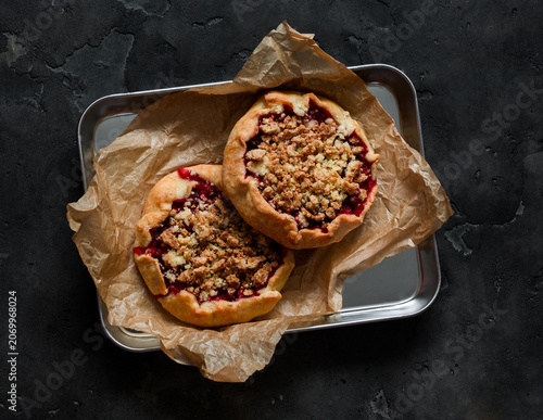 Mini berry galettes with crumble on a metal tray on a dark background, top view