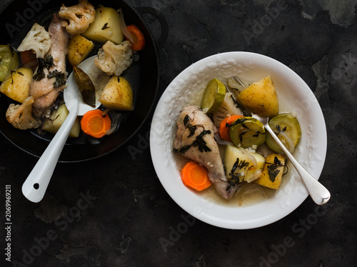 Stewed chicken with potatoes, zucchini, cauliflower and herbs in a cast-iron skillet is a comfortable healthy meal on a dark background, top view