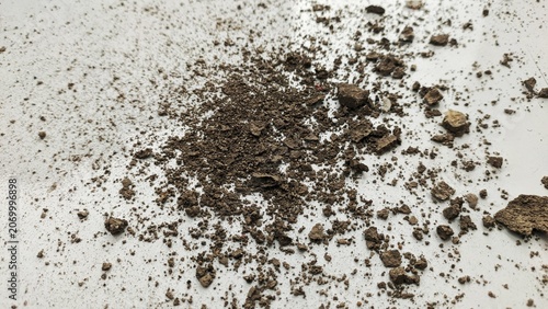 Crushed dry soil pile and dirt debris scattered on a white surface background.