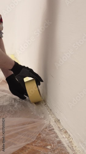 Preparing for painting interior walls using masking tape to attach protective film to the floor inside the room
