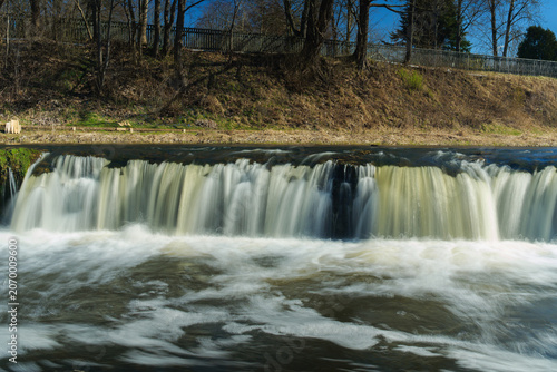 View of Ventas Rumba waterfall flowing over the limestone ledge with trees on the riverbank in Kuldiga, Kuldigas novads, Latvia.