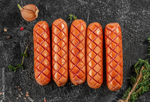 Grilled sausages with cross cut pattern on dark stone background top view
