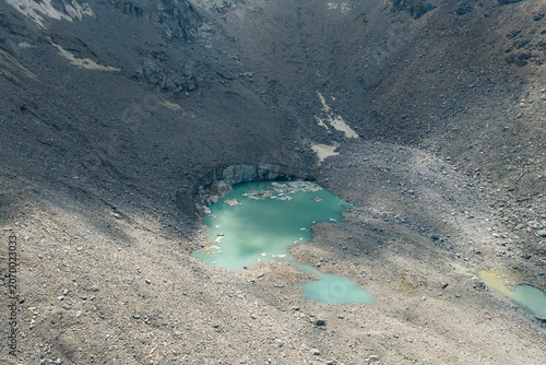 Aerial view of a turquoise glacial lake nestled among rugged rocky slopes and grey scree at Pereval Tossor Jety-Oguz, Issyk-Kul Region, Kyrgyzstan.