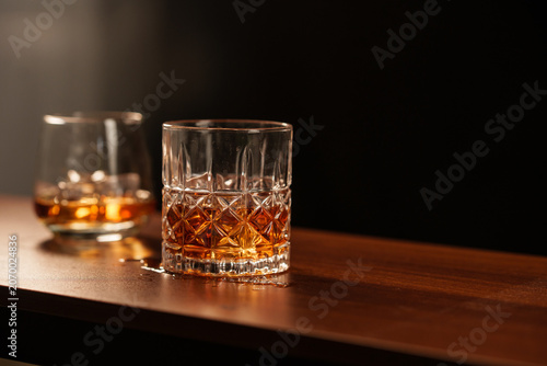 A glass of whisky with ice sits on a wooden table.
