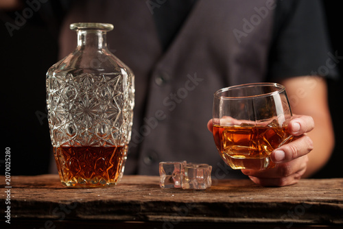 Man in Vest Holding Elegant Whiskey Glass with Crystal Decanter on Rustic Wooden Surface