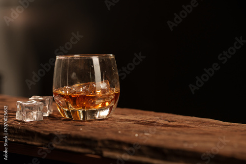 Whiskey glass with ice cubes on rustic wooden surface