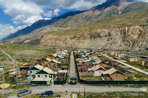 Aerial view of the remote settlement of Enilchek with small houses and a central road nestled against rugged mountain slopes in Enilchek, Issyk-Kul Region, Kyrgyzstan.