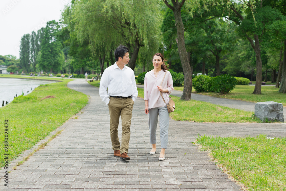 Obraz premium 湖畔の並木道を散歩する40代夫婦