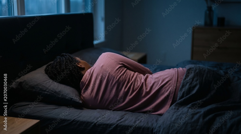 Fototapeta premium African American woman sleeping peacefully in her cozy dark bedroom at night.