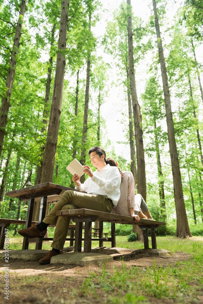 Fototapeta premium 公園のベンチで読書を楽しむ40代夫婦