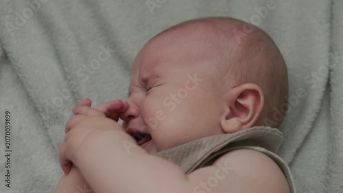 Teething baby lying down, chewing toy and moving hands and feet actively. Top view of sweet infant crying and smiling during first teeth growth milestone. Pediatric and parenting concept.