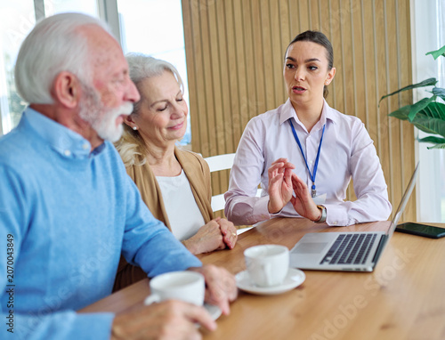 Senior couple having a meeting with an agent, businesswoman, salesperson or doctor using a laptop computer  in his office