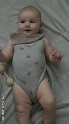 Teething baby lying down, chewing toy and moving hands and feet actively. Top view of sweet infant crying and smiling during first teeth growth milestone. Pediatric and parenting concept.