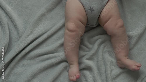 Teething baby lying down, chewing toy and moving hands and feet actively. Top view of sweet infant crying and smiling during first teeth growth milestone. Pediatric and parenting concept.