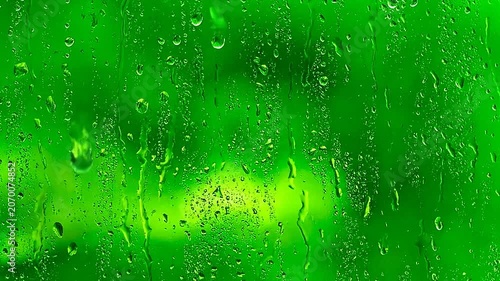 Raindrops falling on a clear glass surface with green background